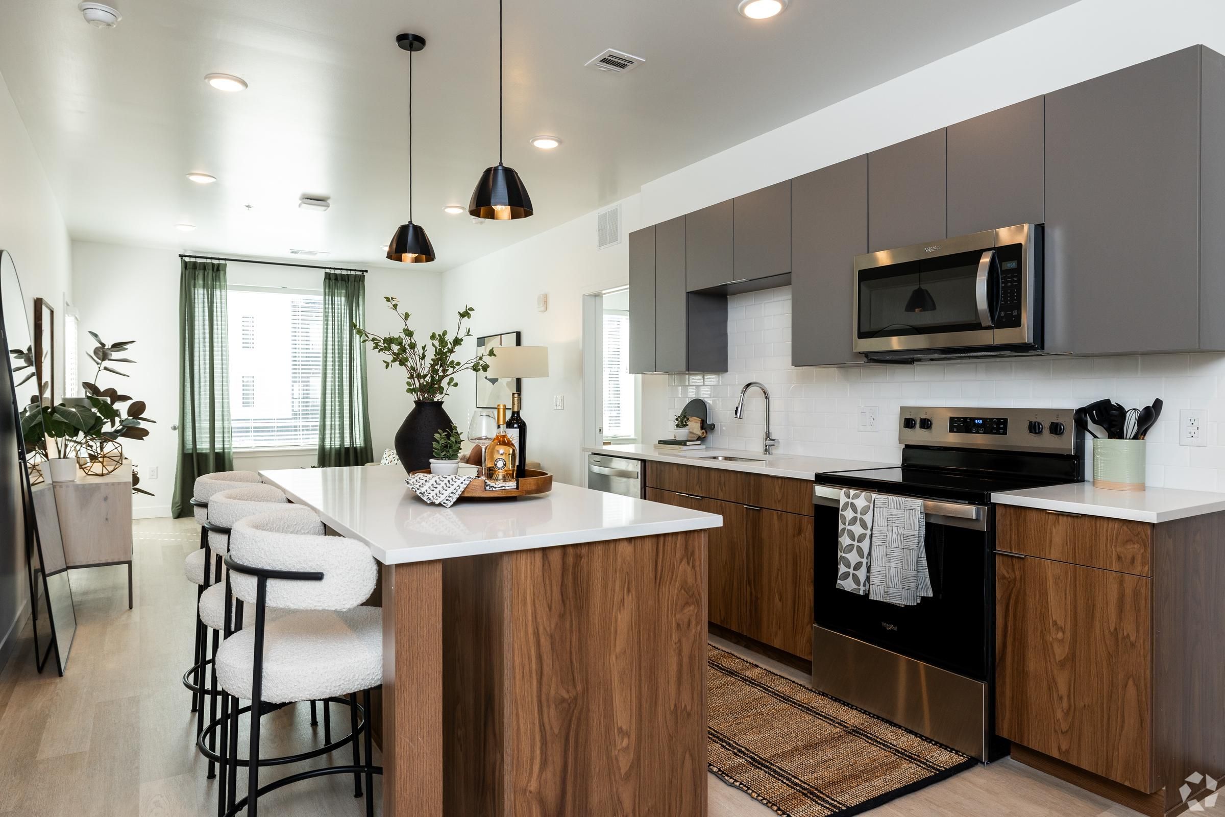 The Oslo kitchen with wood cabinets, white countertops, an island with stools, and stainless steel appliances.