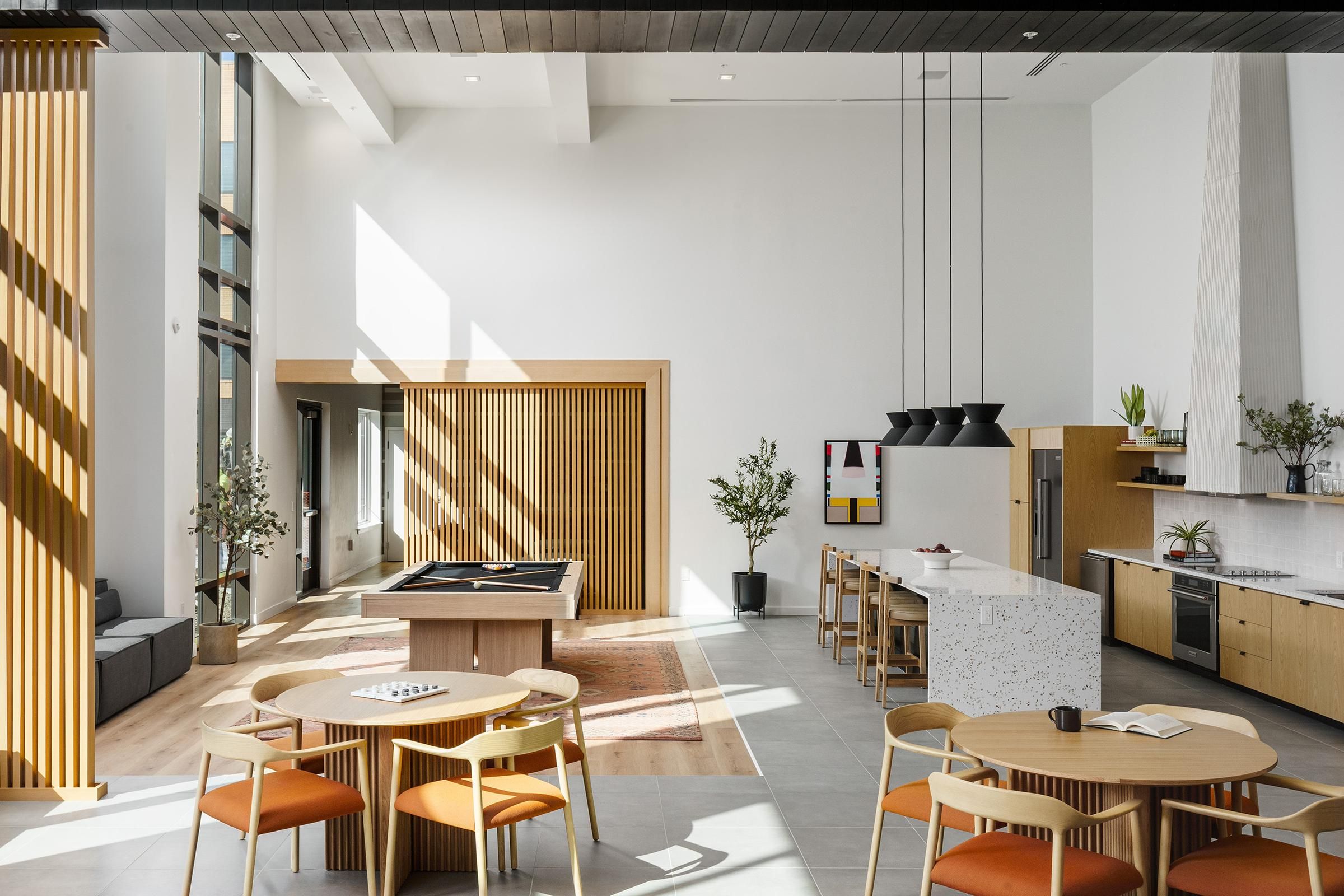 Modern open-concept room with a pool table, dining tables, bar area, and large windows allowing natural light.