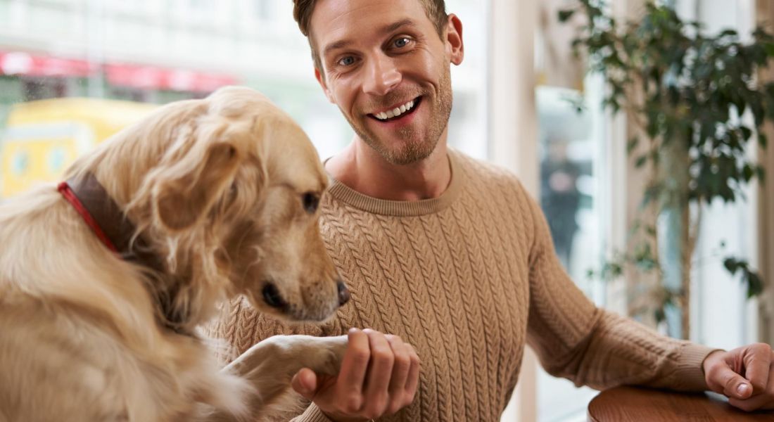 The Oslo A man smiles warmly as he gently pets a dog, showcasing a moment of joy and companionship between them.