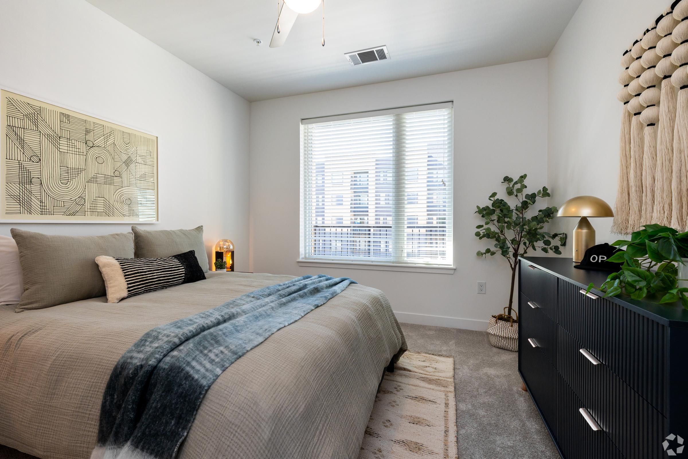 The Oslo bedroom with a neatly made bed, dresser, large window, and minimalistic decor.