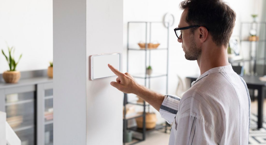 The Oslo A man points at a white wall featuring a modern smart thermostat, demonstrating its functionality and design.