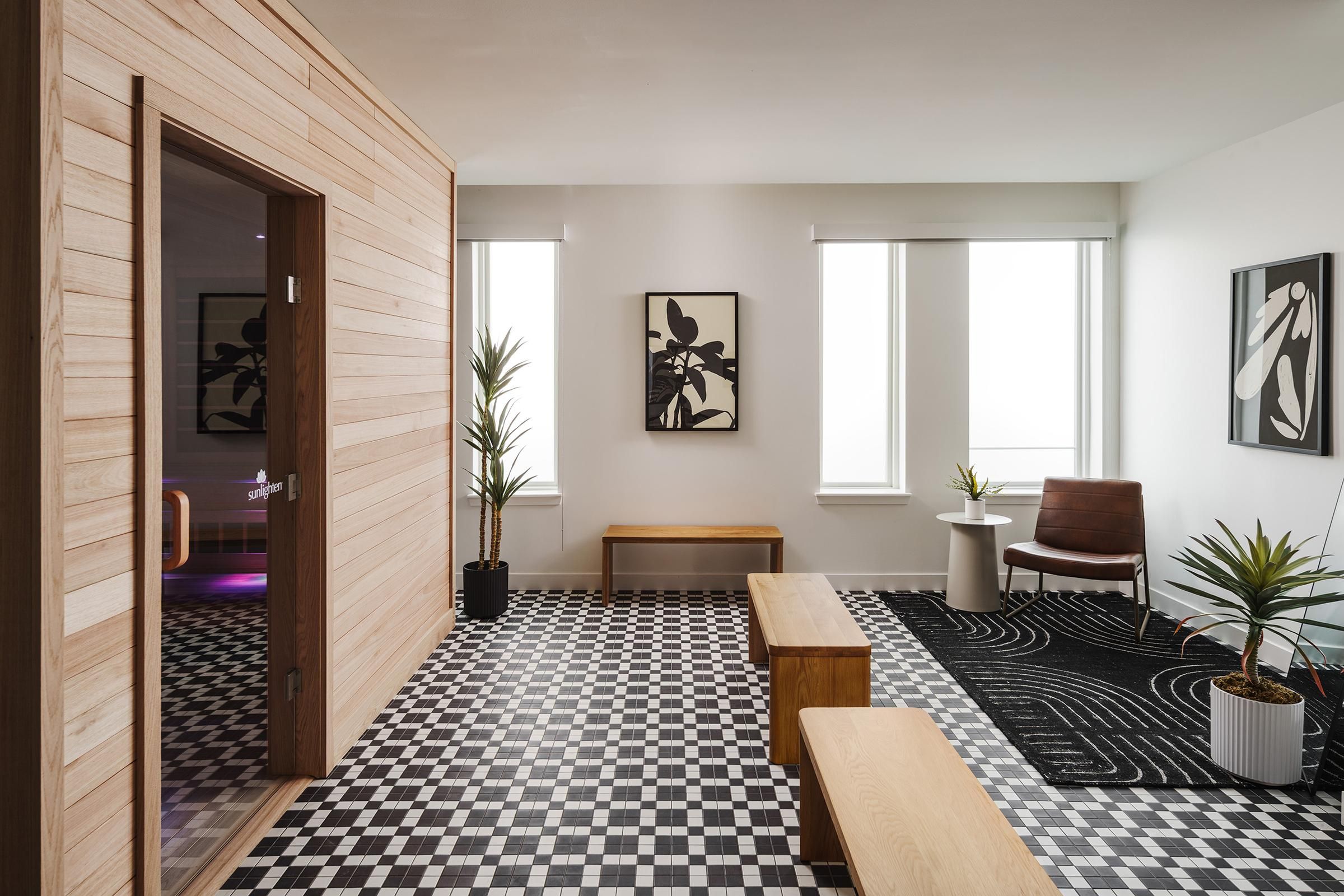 Minimalist room with checkered floor, wooden benches, and abstract art on the wall. Two windows provide natural light.