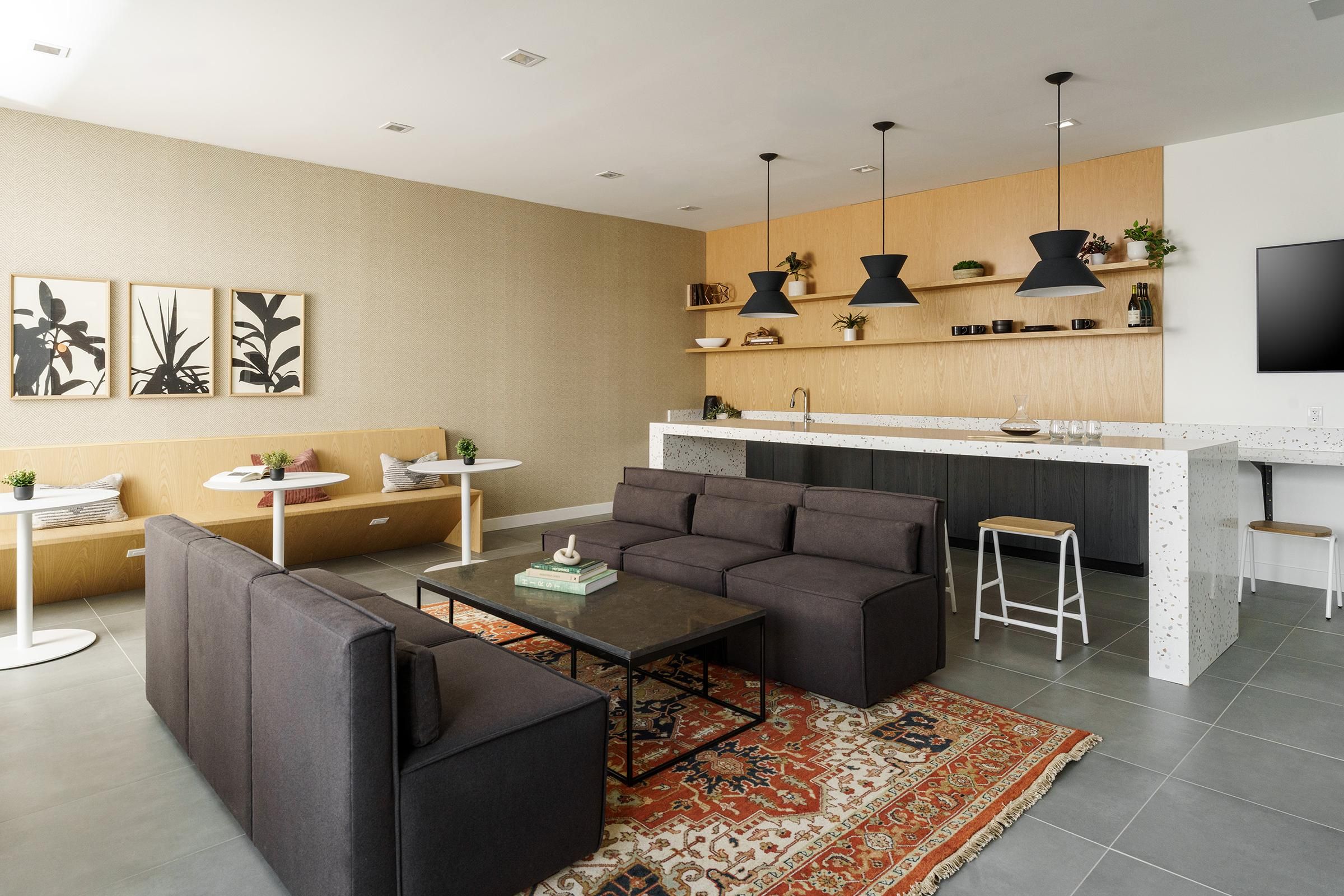Modern living room with dark sofas, a coffee table, wall art, pendant lights, and a kitchen area with stools and shelves.